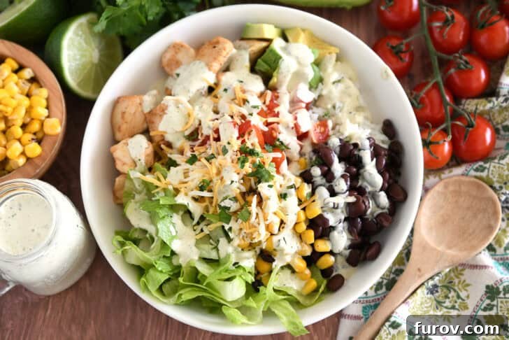 A visually appealing white bowl generously filled with cooked chicken, fresh chopped tomatoes, cilantro lime rice, creamy avocado chunks, black beans, roasted corn, and crisp lettuce, ready for a delicious meal.