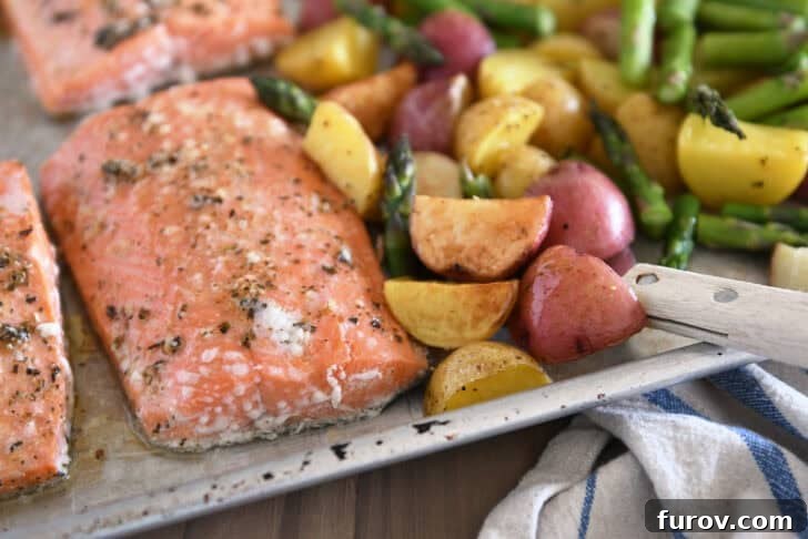 Close-up view of a sheet pan holding a baked piece of lemon garlic salmon, accompanied by golden roasted potatoes and vibrant green asparagus.