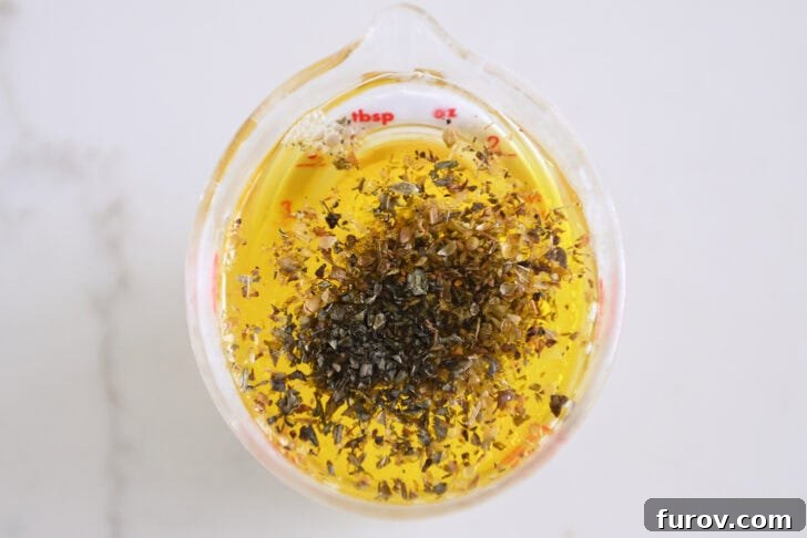 Liquid measuring cup containing a vibrant mix of olive oil, fresh lemon juice, minced garlic, dried oregano, and basil, ready to become a flavorful marinade.