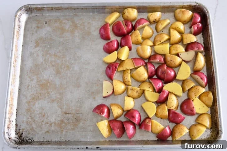 Top-down view of a hot sheet pan generously covered with evenly cut red and yellow potatoes, ready for roasting.