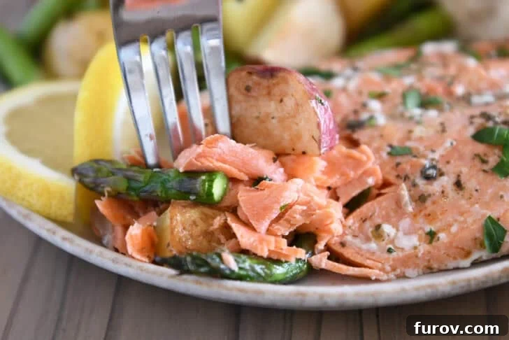 A elegant gray plate presenting a perfectly plated portion of baked salmon, roasted asparagus, and golden potatoes, ready to be enjoyed with a fork.
