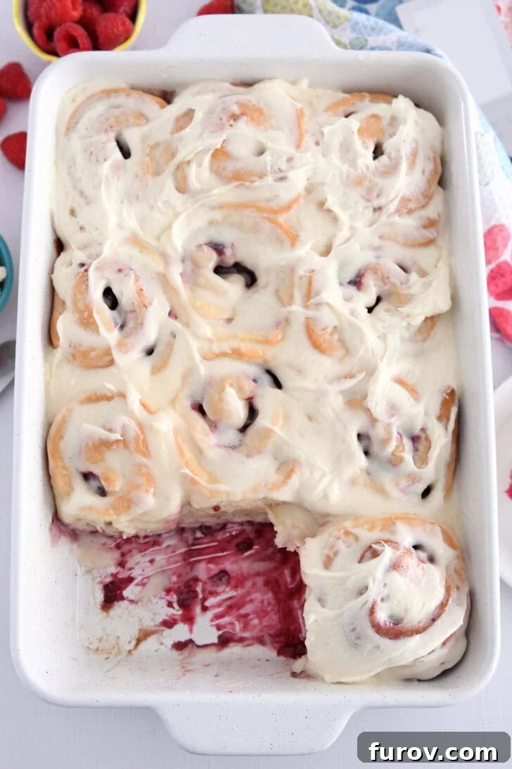White 9X13-inch pan of baked raspberry sweet rolls spread with sweet cream cheese icing.