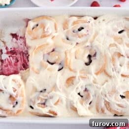 White 9X13-inch pan of baked raspberry sweet rolls spread with sweet cream cheese icing.