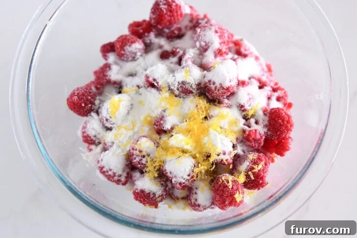 Glass bowl with frozen raspberries, sugar, cornstarch, and lemon zest, ready for the filling.