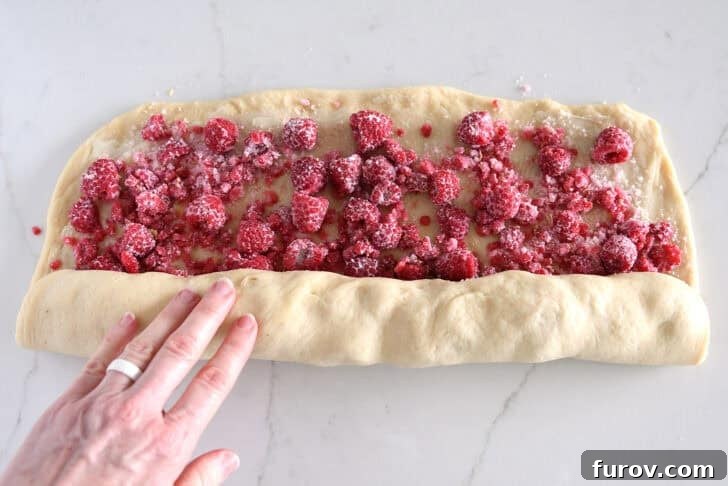Rolling up log of raspberry sweet rolls with sugary raspberry filling.