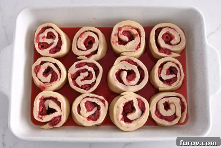 White 9X13-inch pan with rising raspberry sweet rolls.
