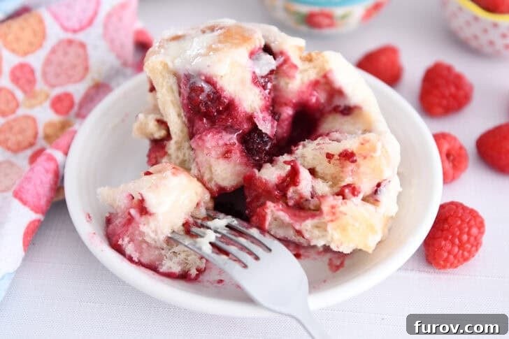 Fork taking piece of raspberry sweet roll on white plate.