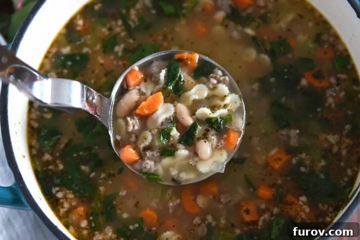 Hearty Italian Sausage White Bean Pasta Soup 3 Ladle lifting serving of soup in pot with small pasta, spinach, carrots, white beans, and sausage.