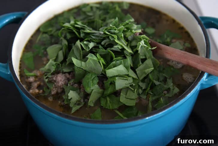 Hearty Italian Sausage White Bean Pasta Soup 7 Large pot with fresh, chopped spinach on top of broth and soup.