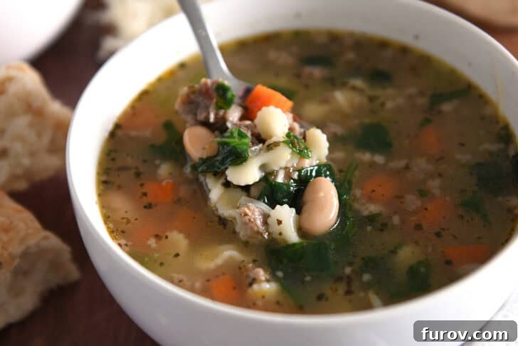 Hearty Italian Sausage White Bean Pasta Soup 8 Spoon lifting bite of soup in white bowl with small pasta, spinach, carrots, white beans, and sausage.