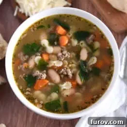 Top down photo of white bowl with broth, carrots, white beans, small pasta, and spinach.