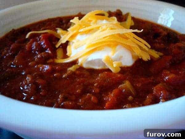 A pristine white bowl filled with creamy, rich chili, beautifully topped with a swirl of sour cream and a generous sprinkle of shredded cheese, ready to be enjoyed.