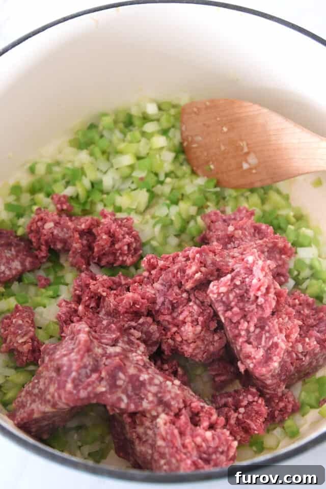 A cast iron pot simmering with savory ground beef, freshly chopped celery, and aromatic onions, forming the rich foundation for a delicious chili.