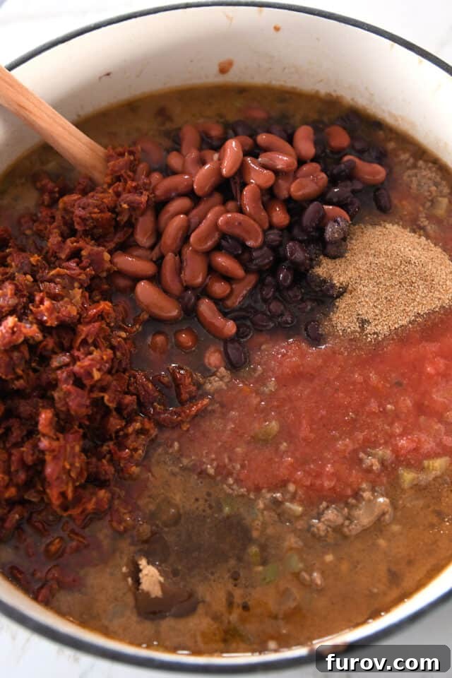 A robust cast iron pot filled with rich beef broth, crushed tomatoes, wholesome black beans, kidney beans, and intensely flavorful sun-dried tomatoes, blending into a hearty chili.