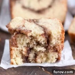 Two half slices of cinnamon swirl quick bread stacked on white parchment paper, highlighting the moist texture and cinnamon swirl.