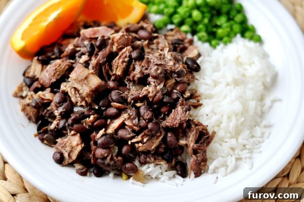 Top view of a plate of shredded pork and black beans, white rice, peas, and orange slices, ready to be enjoyed.
