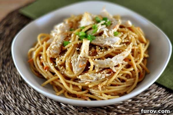 Creamy Peanut Sesame Noodles 2 Sesame noodles topped with succulent shredded chicken and vibrant green onions, served in an elegant white bowl.