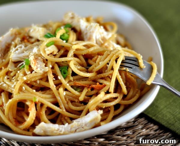 Creamy Peanut Sesame Noodles 3 A white dish showcasing perfectly cooked pasta and tender shredded chicken, generously sprinkled with aromatic sesame seeds and fresh green onions.