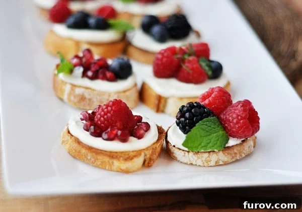A white tray brimming with colorful sweet berry bruschetta appetizers, featuring pomegranate, raspberries, blackberries, and blueberries.