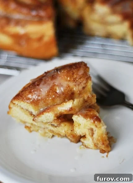 Mastering Giant Cinnamon Rolls A Step by Step Photo Guide 3 A generously sized, pie-shaped slice of a giant cinnamon roll, drizzled with glaze, presented on a pristine white plate.