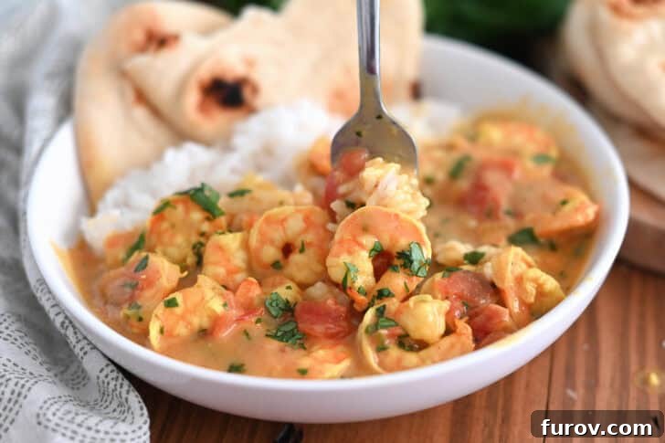 A fork taking a bite of rice and shrimp curry out of a white bowl with flatbread on the side, highlighting the appetizing texture.