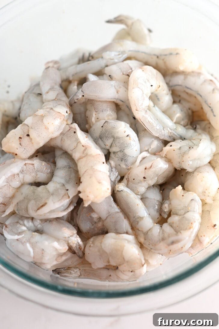 Top down view of raw shrimp in a glass bowl, perfectly seasoned and ready for cooking.