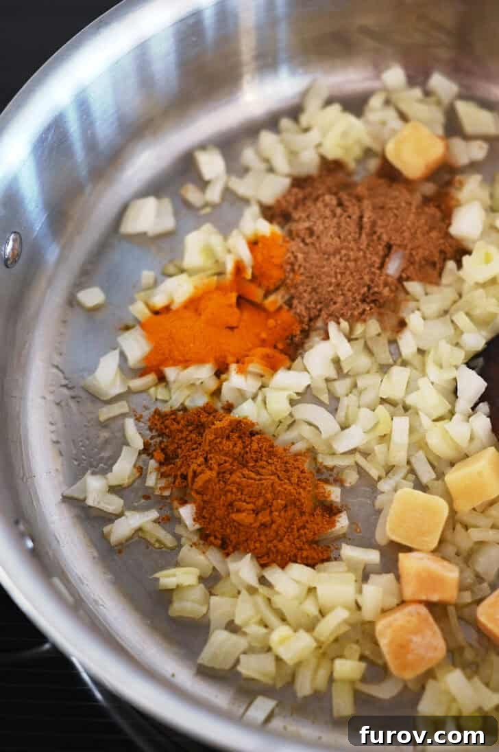 Top down view of a metal pot with diced onions and a vibrant mix of curry spices, sizzling gently to release their aromas.