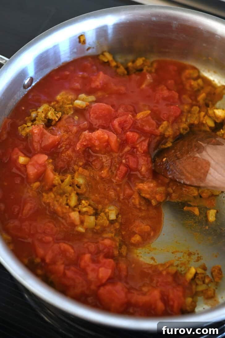 Diced tomatoes, curry spices, and onions cooking together in a metal pot, creating a rich and fragrant base for the curry.