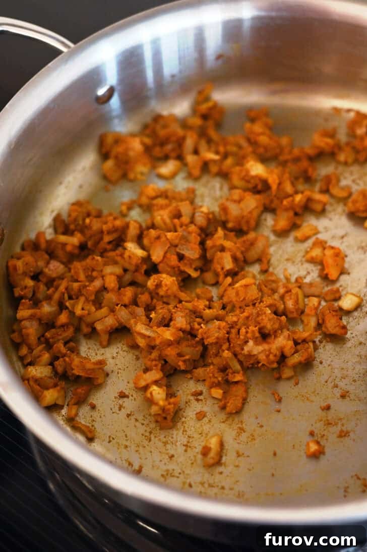 Curry spices and onions cooking in a metal pot, illustrating the texture and color development of the curry base.
