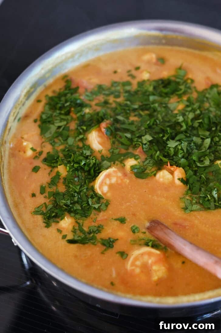 Top down view of a shrimp curry in a metal pot with freshly chopped cilantro on top, adding a bright, finishing touch.