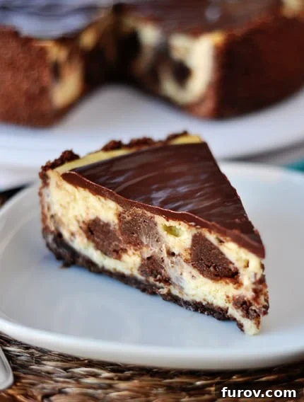 Brownie Patchwork Cheesecake 2 A slice of creamy brownie mosaic cheesecake topped with glossy chocolate ganache on a white plate, highlighting the delightful brownie chunks.