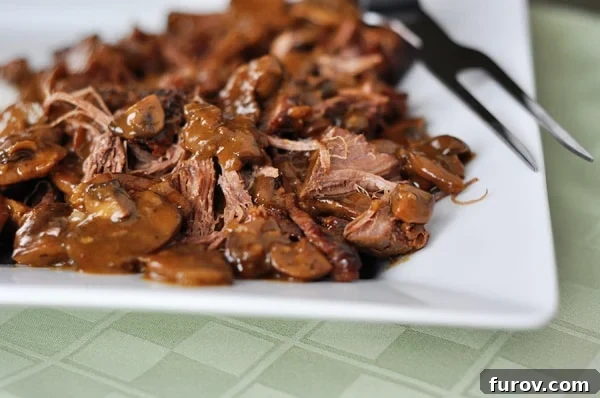Melt-in-Your-Mouth Brisket with Earthy Mushrooms 2 Shredded braised brisket on a white platter, ready to be served, highlighting its tender texture and rich color.