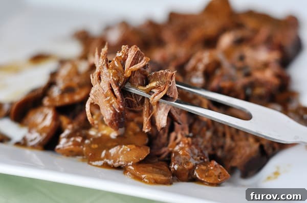Melt-in-Your-Mouth Brisket with Earthy Mushrooms 3 A fork lifts a generous bite of shredded braised brisket and mushroom gravy from a white platter, emphasizing its readiness to eat.