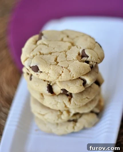 A stack of three gooey, egg-free chocolate chip cookies with visible melted chocolate, placed on a white rectangular platter.