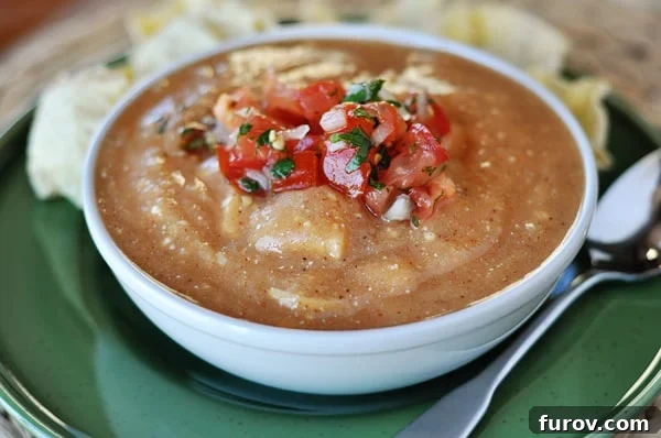 A beautifully plated white bowl of creamy chicken enchilada soup, generously topped with vibrant homemade pico de gallo, ready to be enjoyed as a hearty meal.