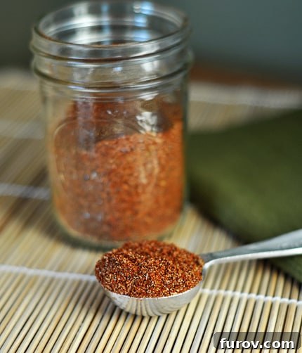 Homemade taco seasoning in a mason jar and scooped in a silver tablespoon in front of the jar.