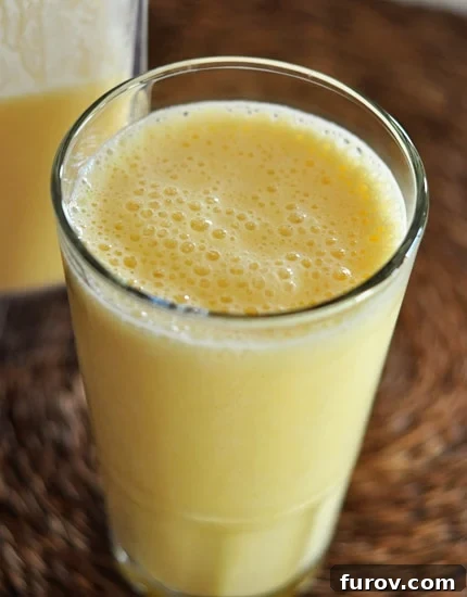 A tall glass cup filled with a frothy orange julius drink, garnished with an orange slice and a straw, sitting on a wooden surface.