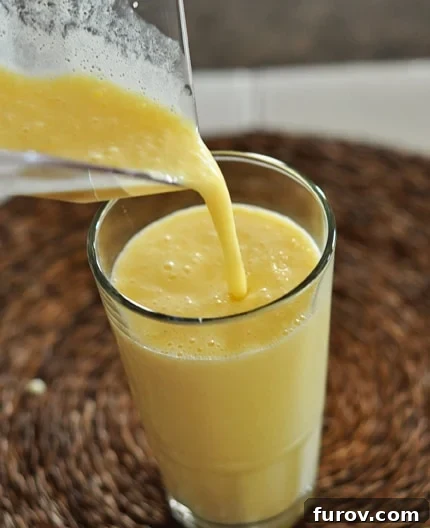 A frothy orange julius mixture being poured from a blender into a tall glass cup, highlighting its smooth and creamy texture.