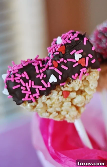 Chocolate-Dipped Krispie Hearts 2 Heart-shaped, chocolate-dipped and sprinkle-topped rice krispie treat on a white stick, perfect for Valentine's Day.