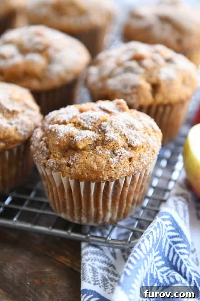 Several baked pumpkin apple spice muffins cooling on a wire rack, with a blue and white striped kitchen towel nearby, evoking a cozy autumn scene.