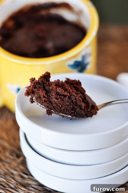 A spoonful of chocolate mug cake on a stack of white plates. The cake is moist and ready to be enjoyed.