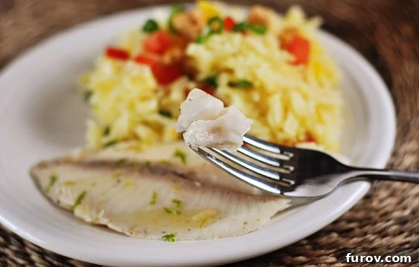 A white plate featuring a perfectly cooked tilapia fillet, with a fork holding a single bite of fish, and a generous serving of vibrant orange jasmine rice artfully arranged behind it. The dish is garnished with fresh herbs, highlighting its freshness and appeal.