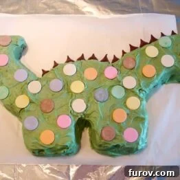 Frosted dinosaur cake with chocolate spikes and colored spots.