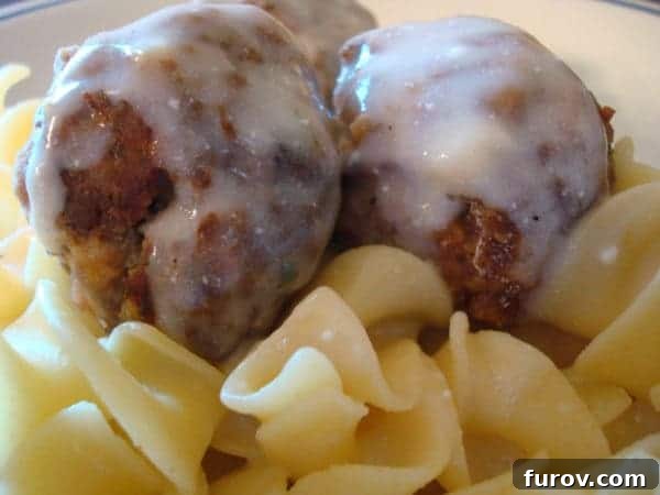 Creamy meatballs elegantly presented on a bed of pasta, generously coated with a rich, white sauce.
