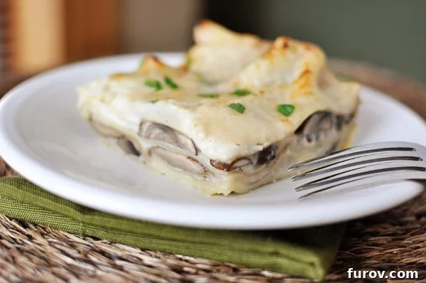 A generous slice of creamy mushroom lasagna with white sauce, beautifully layered and garnished with fresh herbs, resting on a white plate.