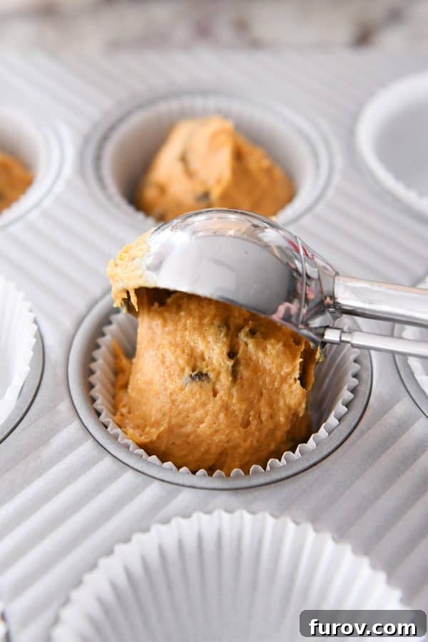 Heavenly Pumpkin Chocolate Chip Muffins 6 Muffin batter being scooped precisely into paper liners set in a muffin tin, ready for baking.
