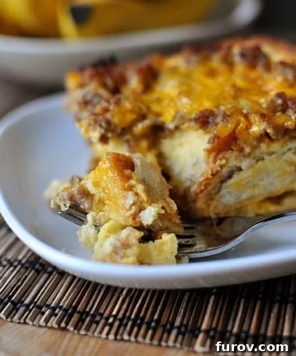 Savory Sausage and Egg Breakfast Strata 2 White plate with a piece of sausage and egg breakfast bake and a fork taking a bite out.