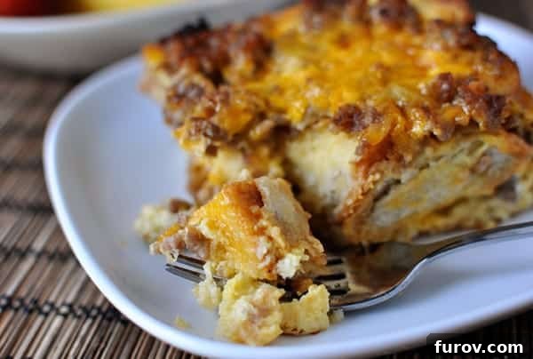 Savory Sausage and Egg Breakfast Strata 3 A square piece of sausage and egg breakfast casserole on a white plate with a fork taking one bite out.