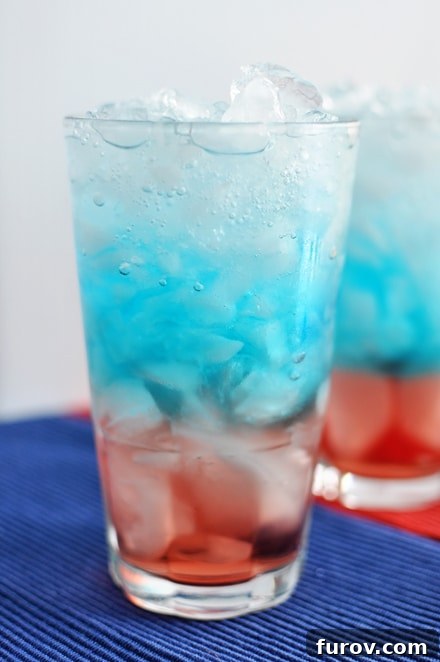 A vibrant red, white, and blue layered drink with ice in a tall glass, perfect for patriotic celebrations.