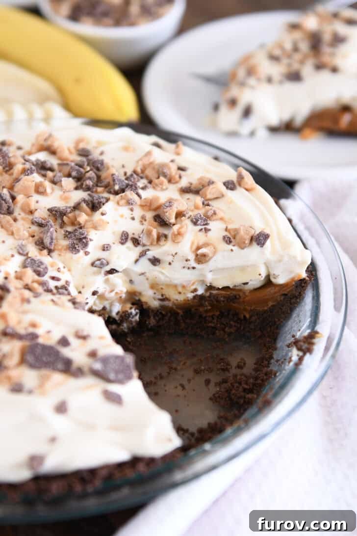 A beautiful Banoffee Pie with one slice removed, showcasing its layers of chocolate crust, dulce de leche, bananas, and cream. The slice sits on a white plate, inviting a taste.